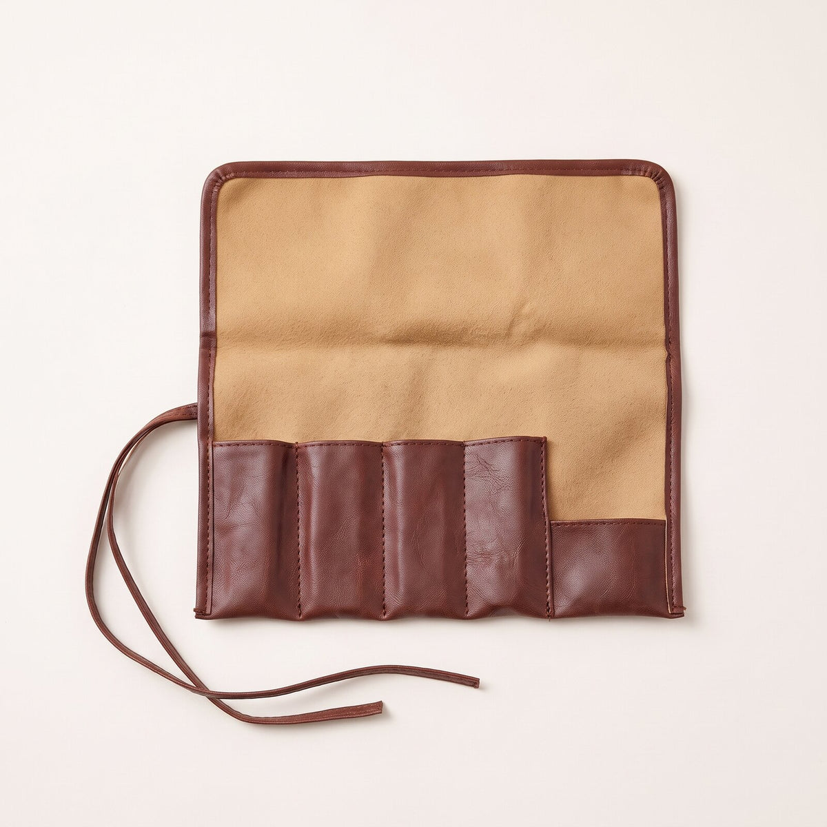 The empty brown roll-up case opened flat, showing its lining, its pockets and a tie cord.