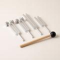 Four tuning forks, two weighted and two plain, and a wooden mallet on warm paper.