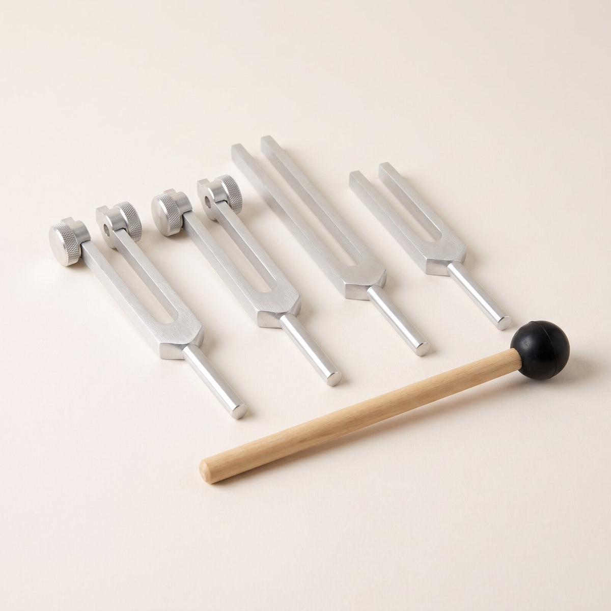 Four tuning forks, two weighted and two plain, and a wooden mallet on warm paper.
