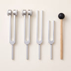 Four tuning forks and a wooden mallet laid out in a row, seen from above.
