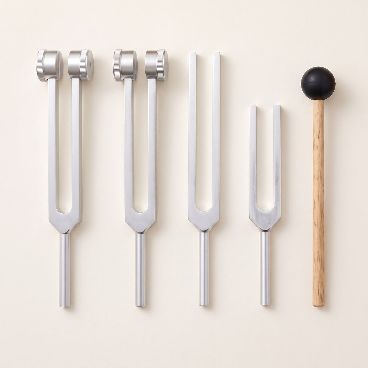 Four tuning forks and a wooden mallet laid out in a row, seen from above.