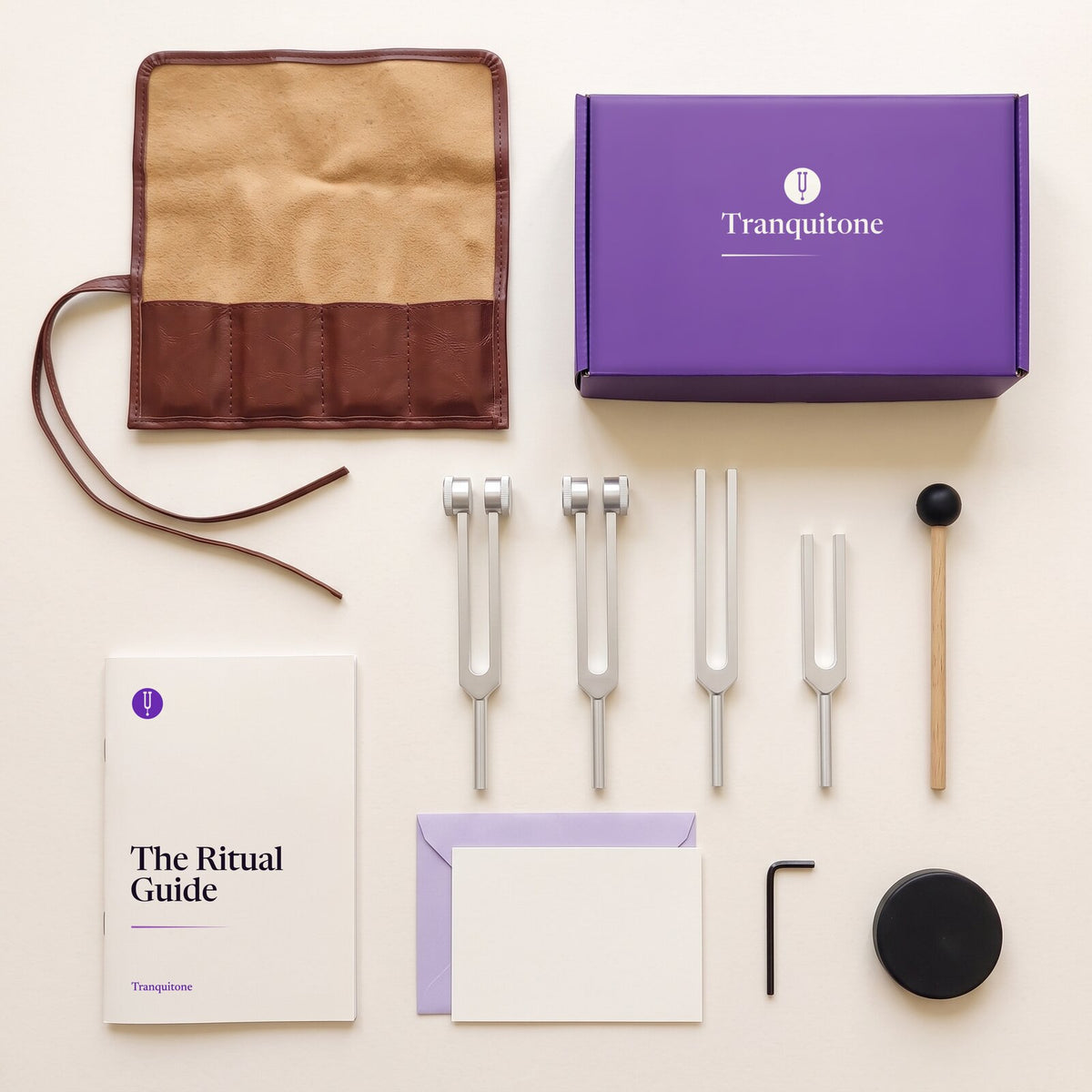 Everything in The Gift Set laid out from above: the open roll-up case, the gift box, four tuning forks, a mallet, The Ritual Guide, a note card and envelope, a small key and a black striking puck.