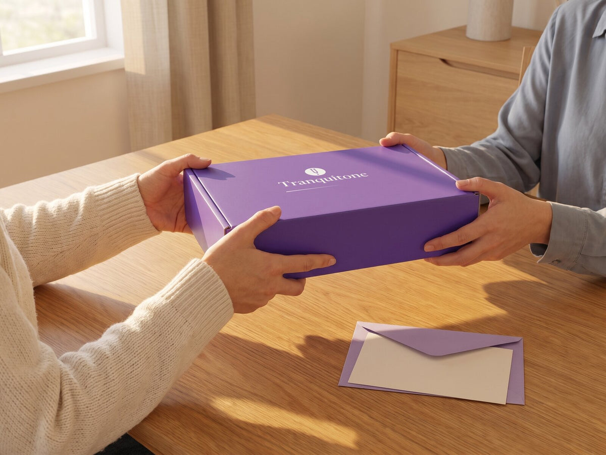 One person hands the Tranquitone gift box to another across a sunny table, an envelope with a blank card below.