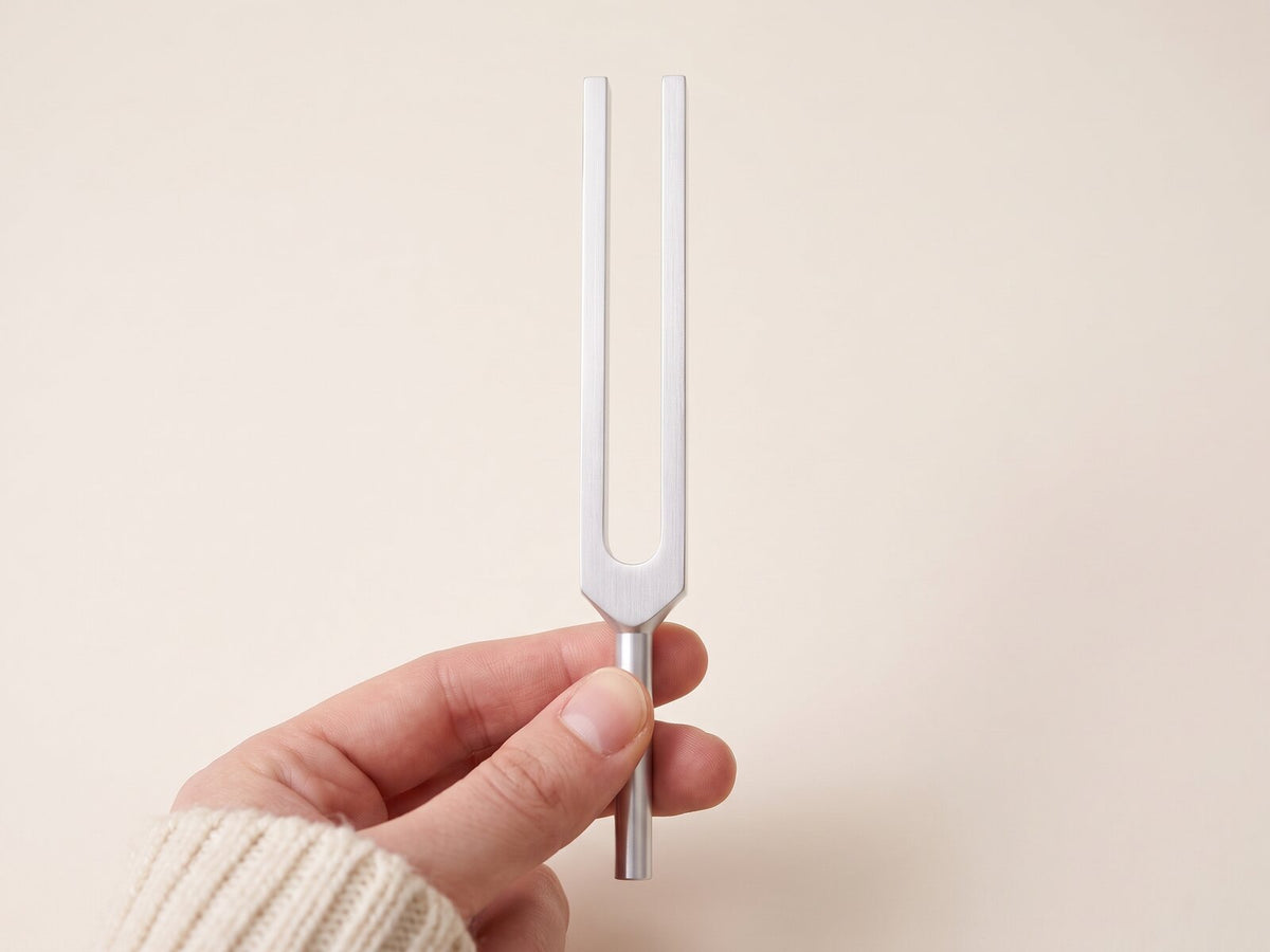 A hand holds a tuning fork by its stem, fingers clear of the prongs.