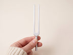 A hand holds a tuning fork by its stem, fingers clear of the prongs.