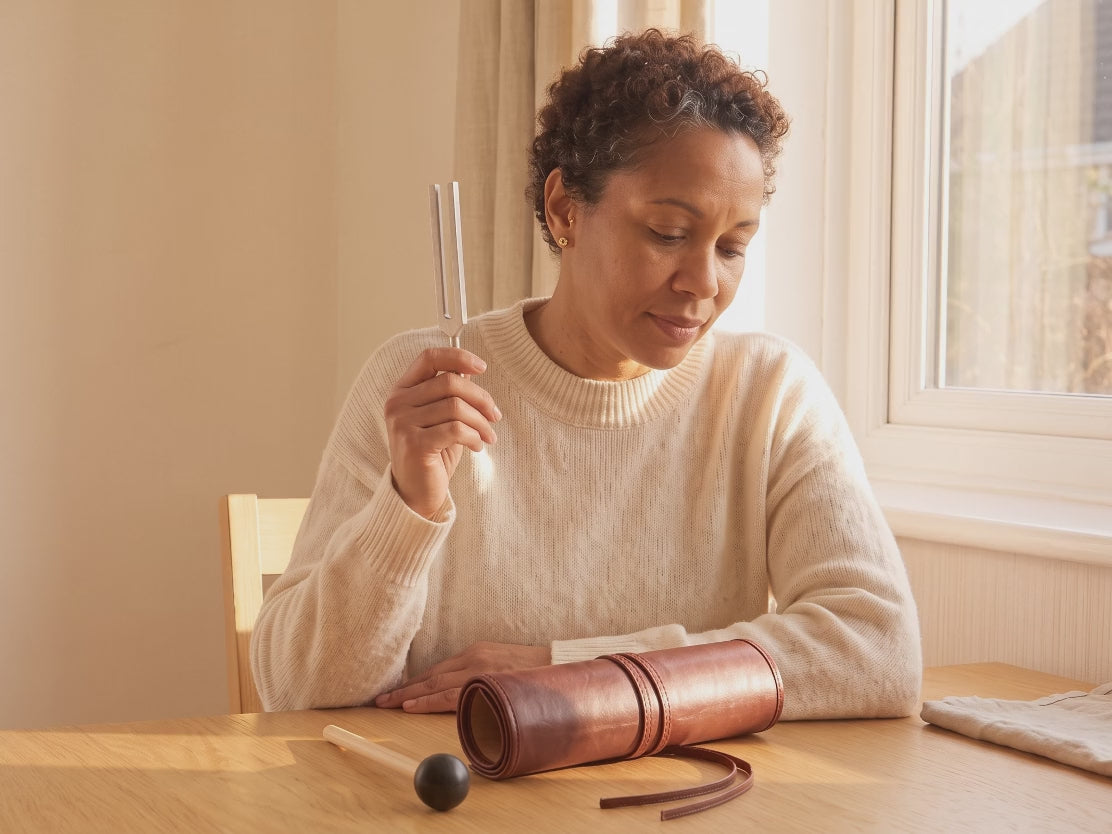 A woman holds a tuning fork beside her ear, with a gap between the fork and her ear.