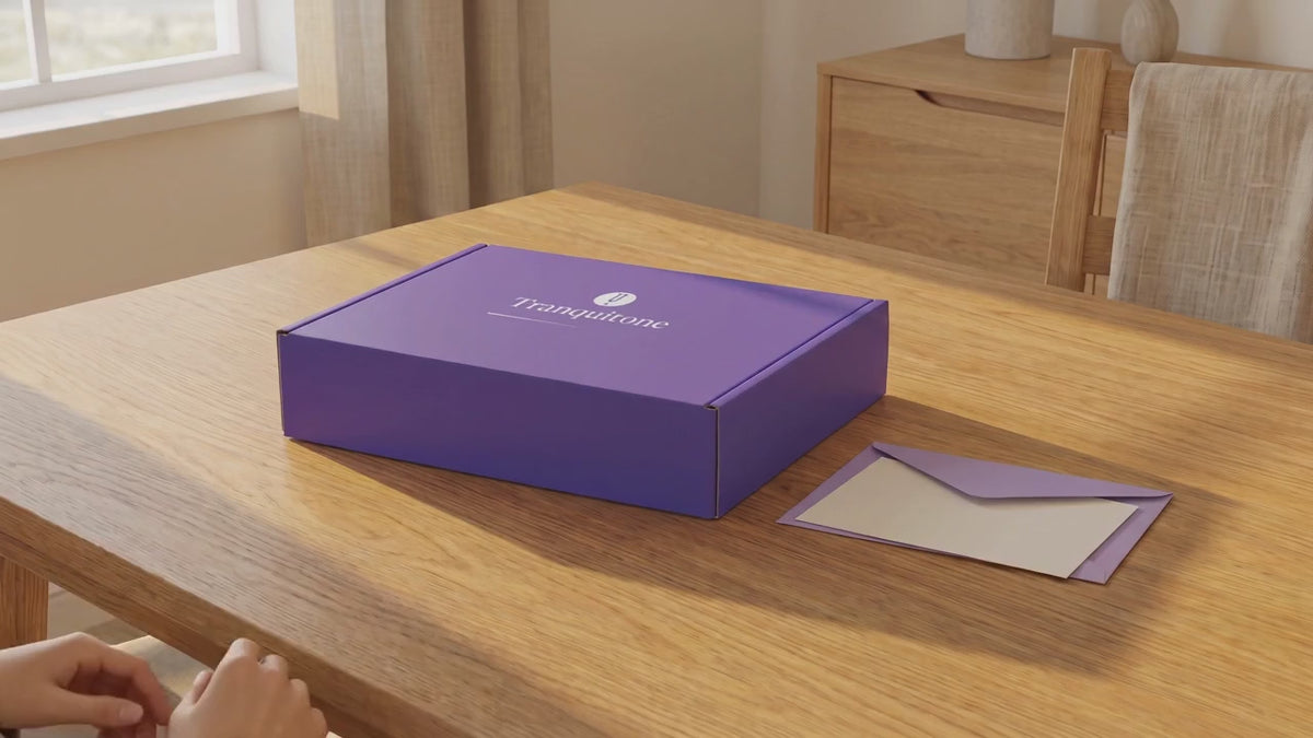Two hands lift the lid of the Tranquitone gift box to show the folded case and the striking puck inside.