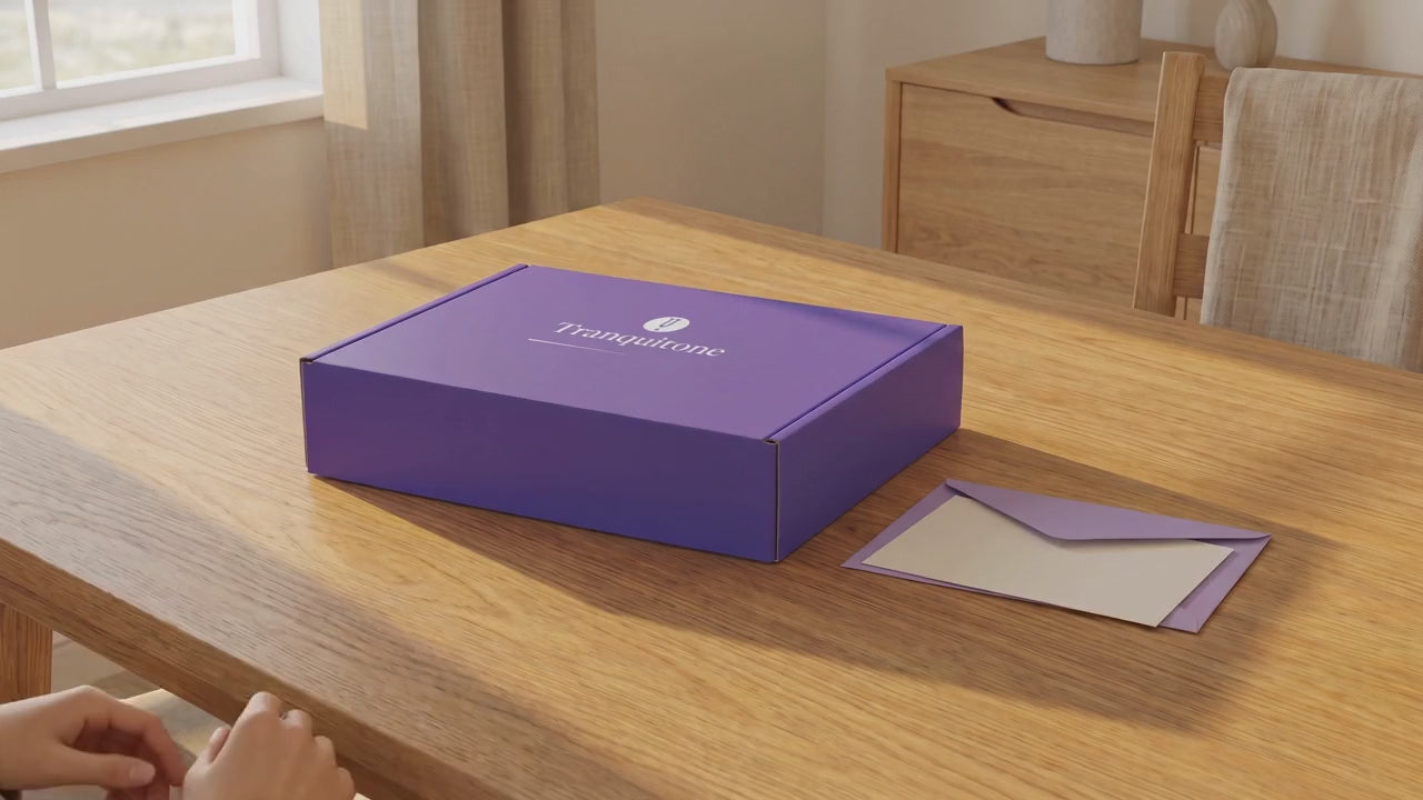 Two hands lift the lid of the Tranquitone gift box to show the folded case and the striking puck inside.
